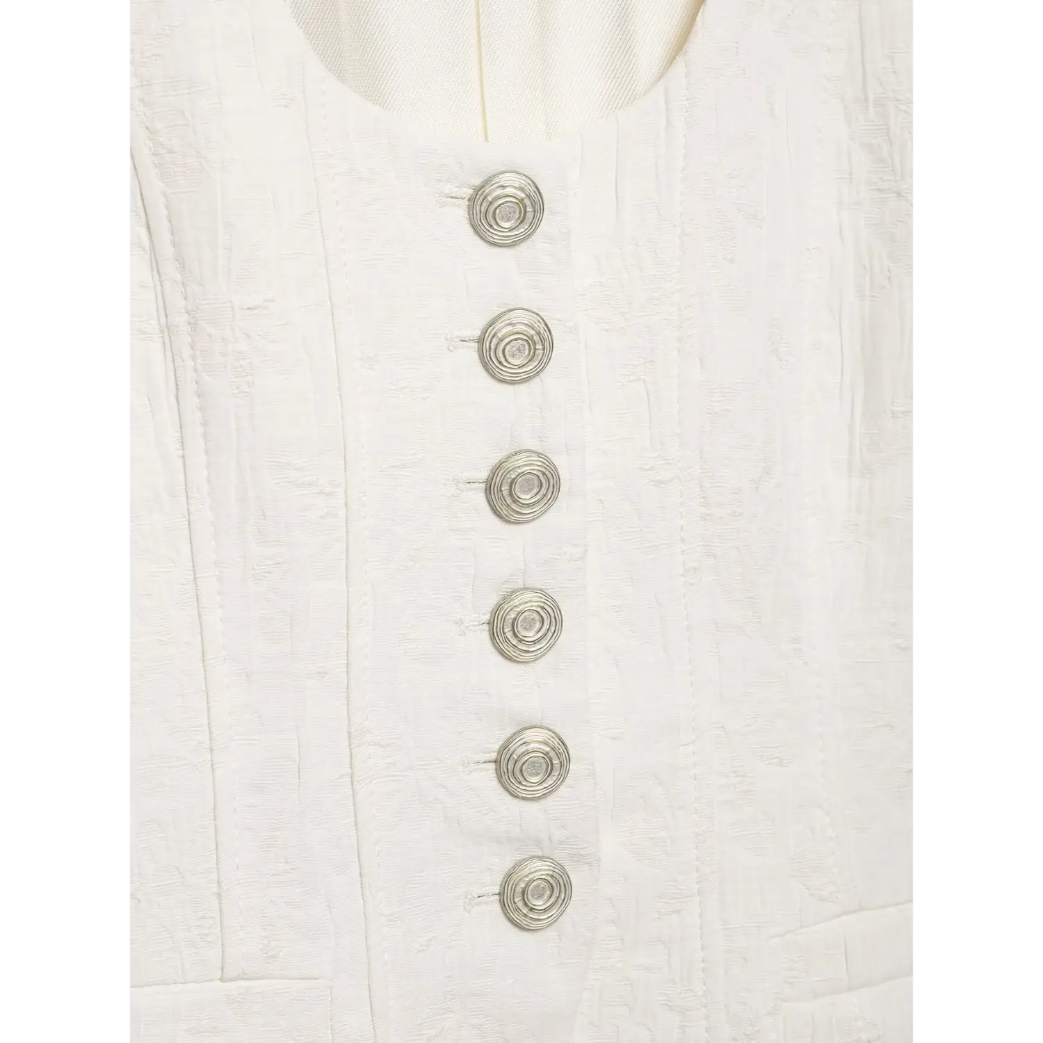 Macro close‑up of decorative silver spiral metal buttons on white textured cropped jacket, embossed jacquard fabric background