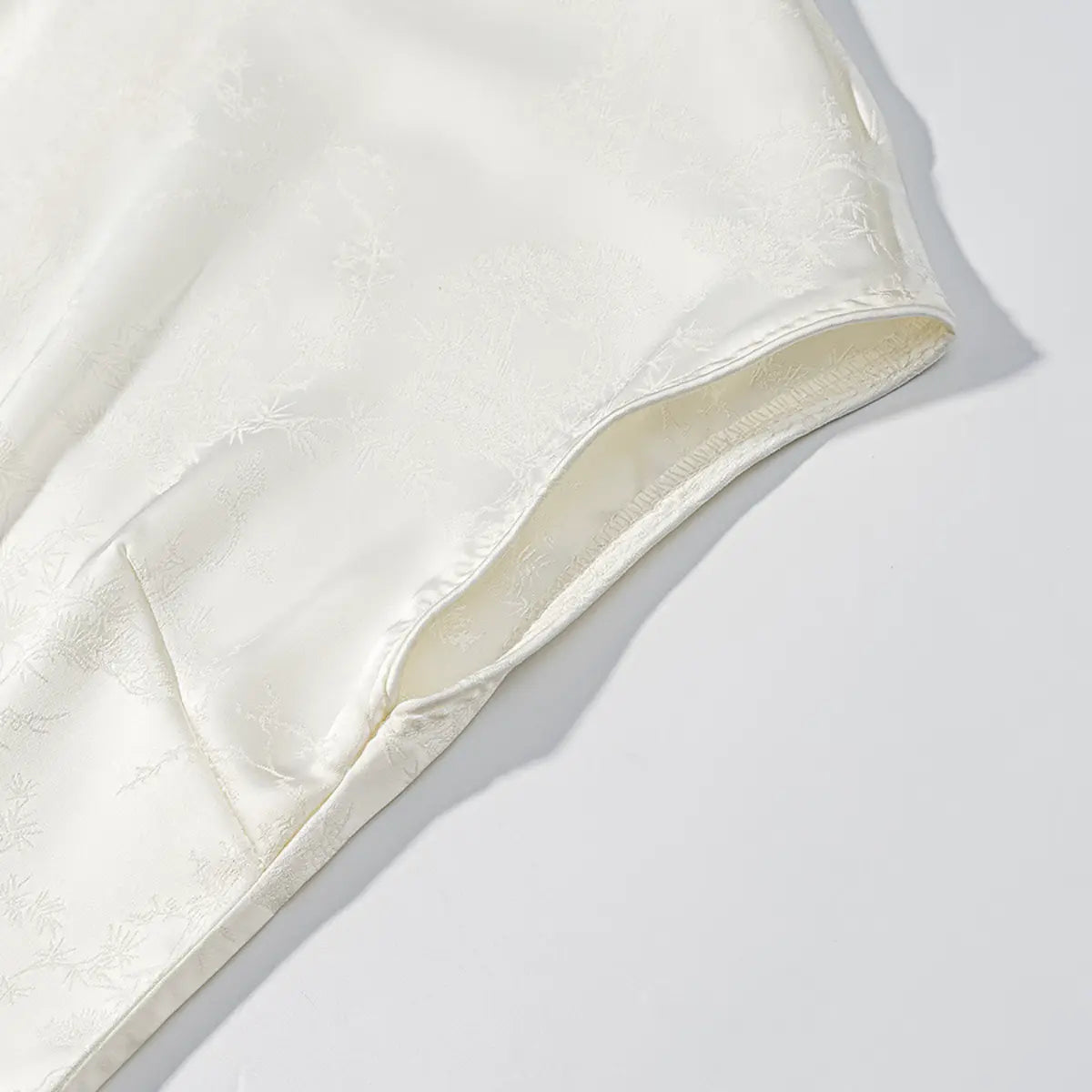 Armhole and shoulder detail of white cheongsam dress, showing the clean stitching and jacquard lining