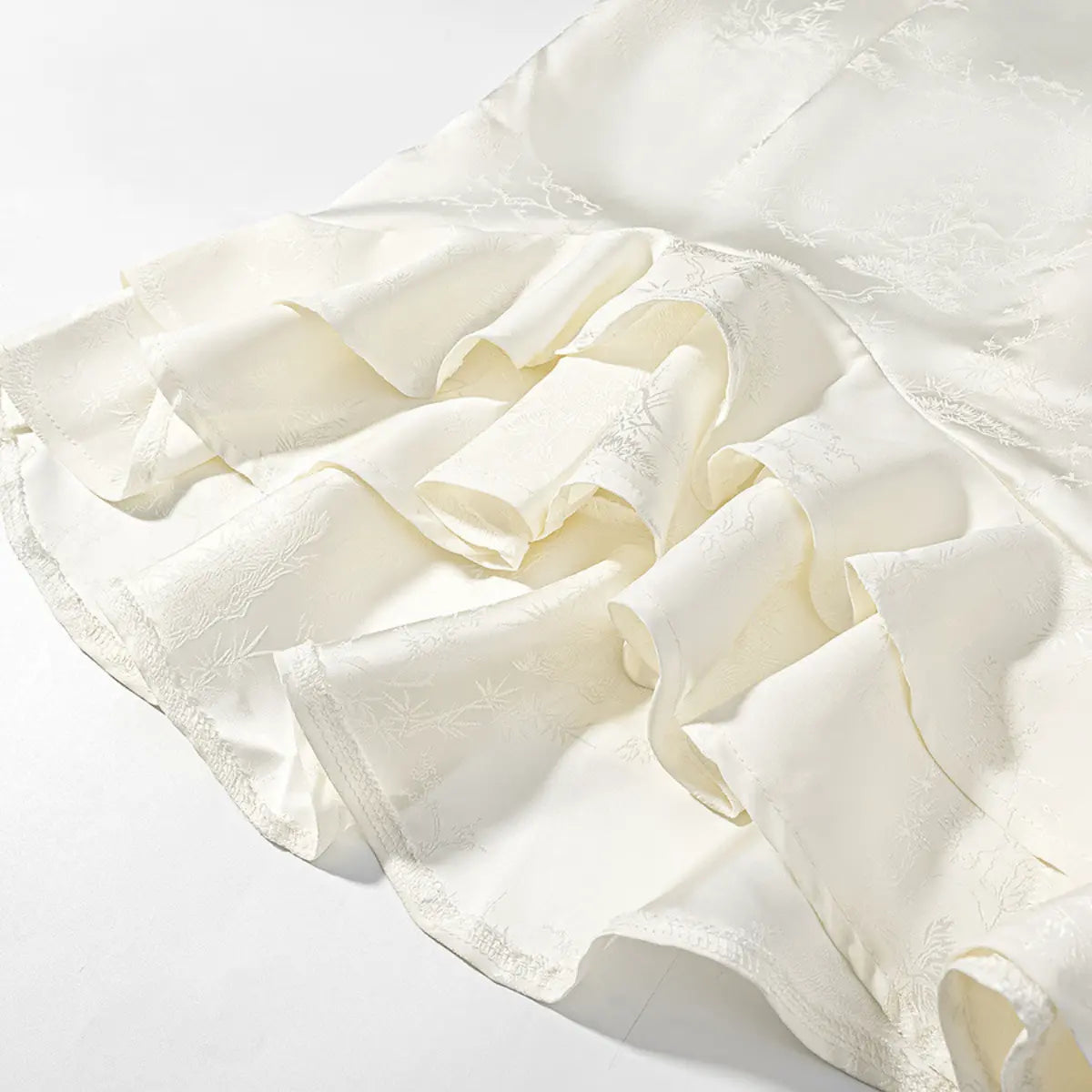 Hem detail of white jacquard cheongsam dress, showing the layered ruffle skirt and bamboo-pattern fabric