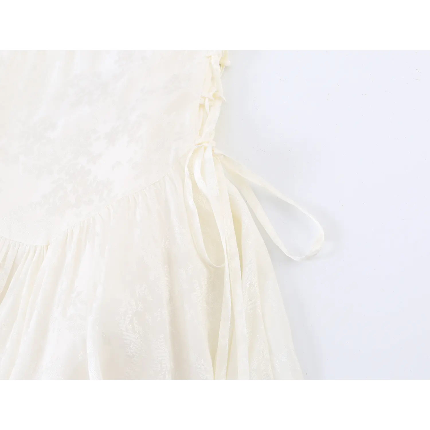 Waist side ribbon tie detail of cream jacquard mini dress, adjustable hanging drawstring with flowy skirt gathering