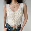 Model wearing white lace‑up cami top, scalloped lace trim, ruched bodice, cropped peplum hem, paired with blue jeans, studio setting