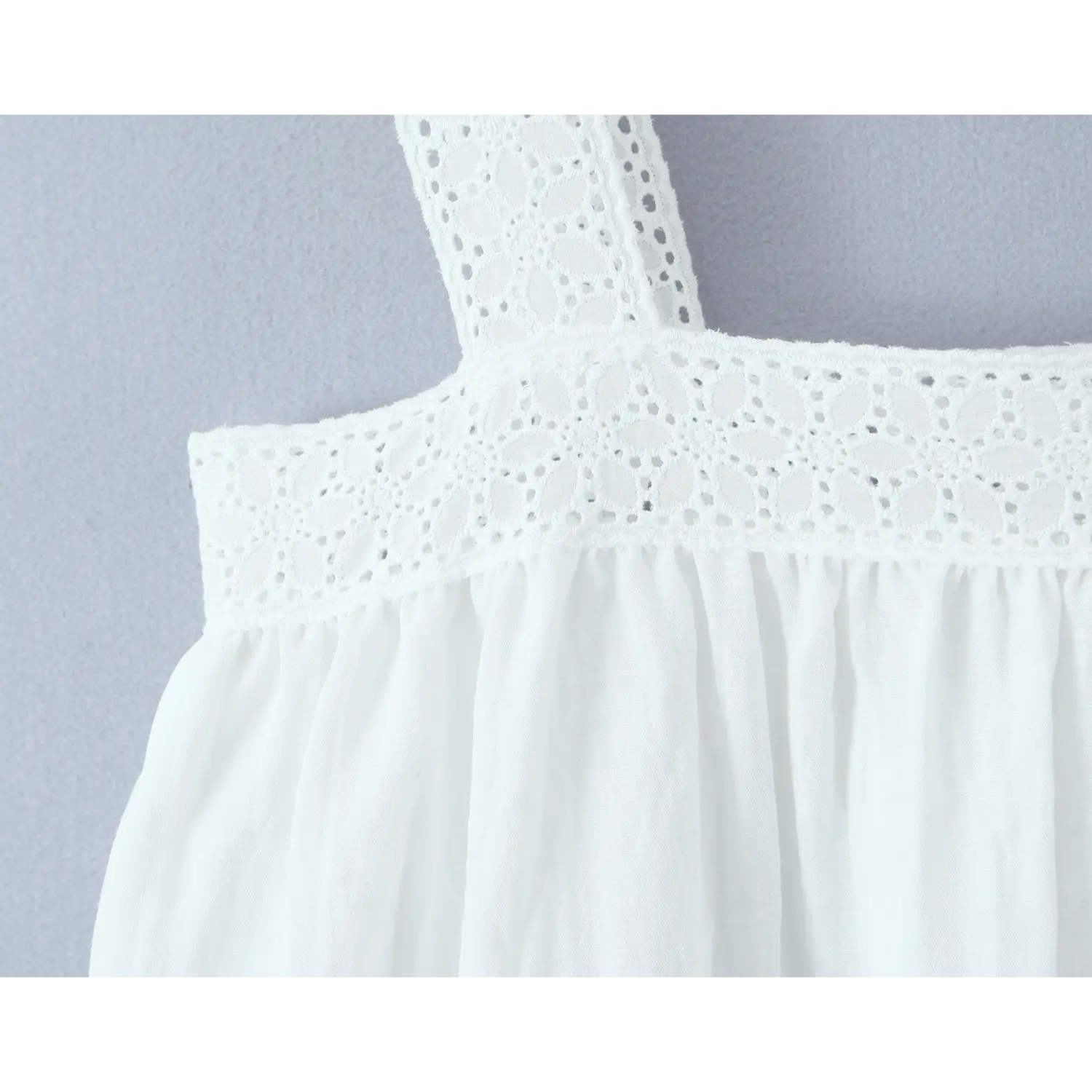 Macro close-up of floral eyelet lace trim fabric on white square neck camisole top