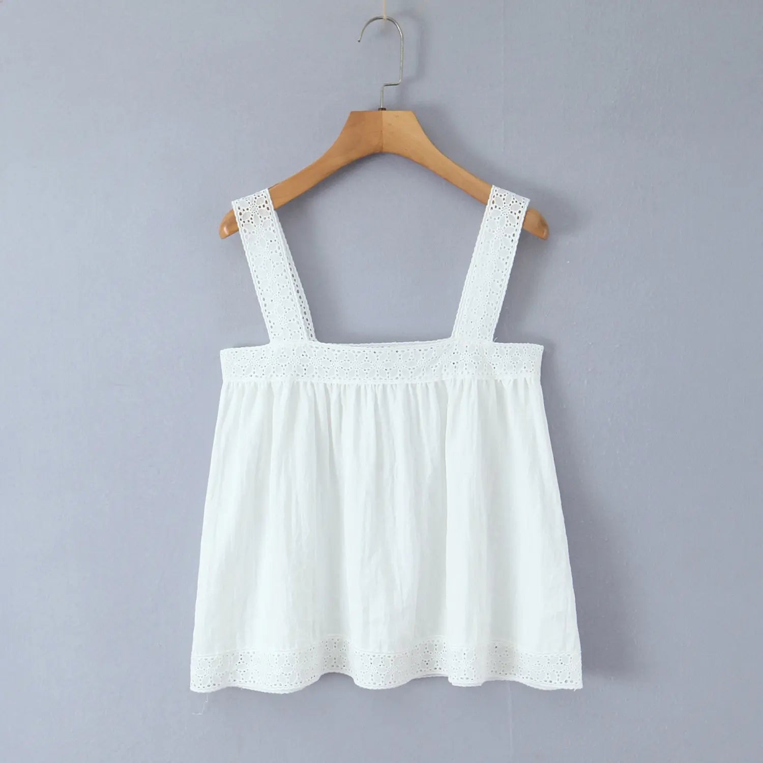 White lace square strap loose camisole hanging on wooden hanger against light grey wall, flat display shot