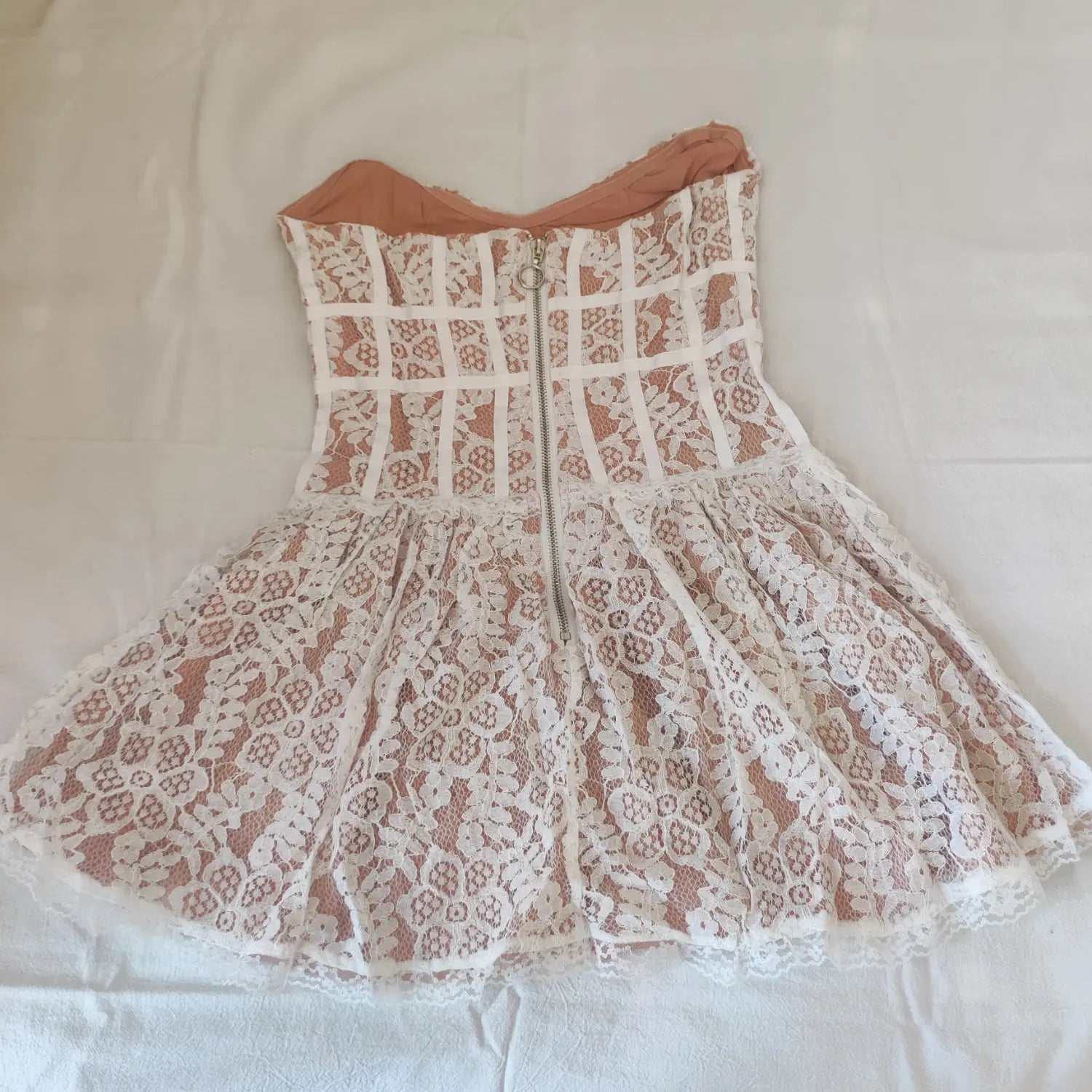 Flat lay back view, white lace strapless corset mini dress with back metal zipper and nude lining