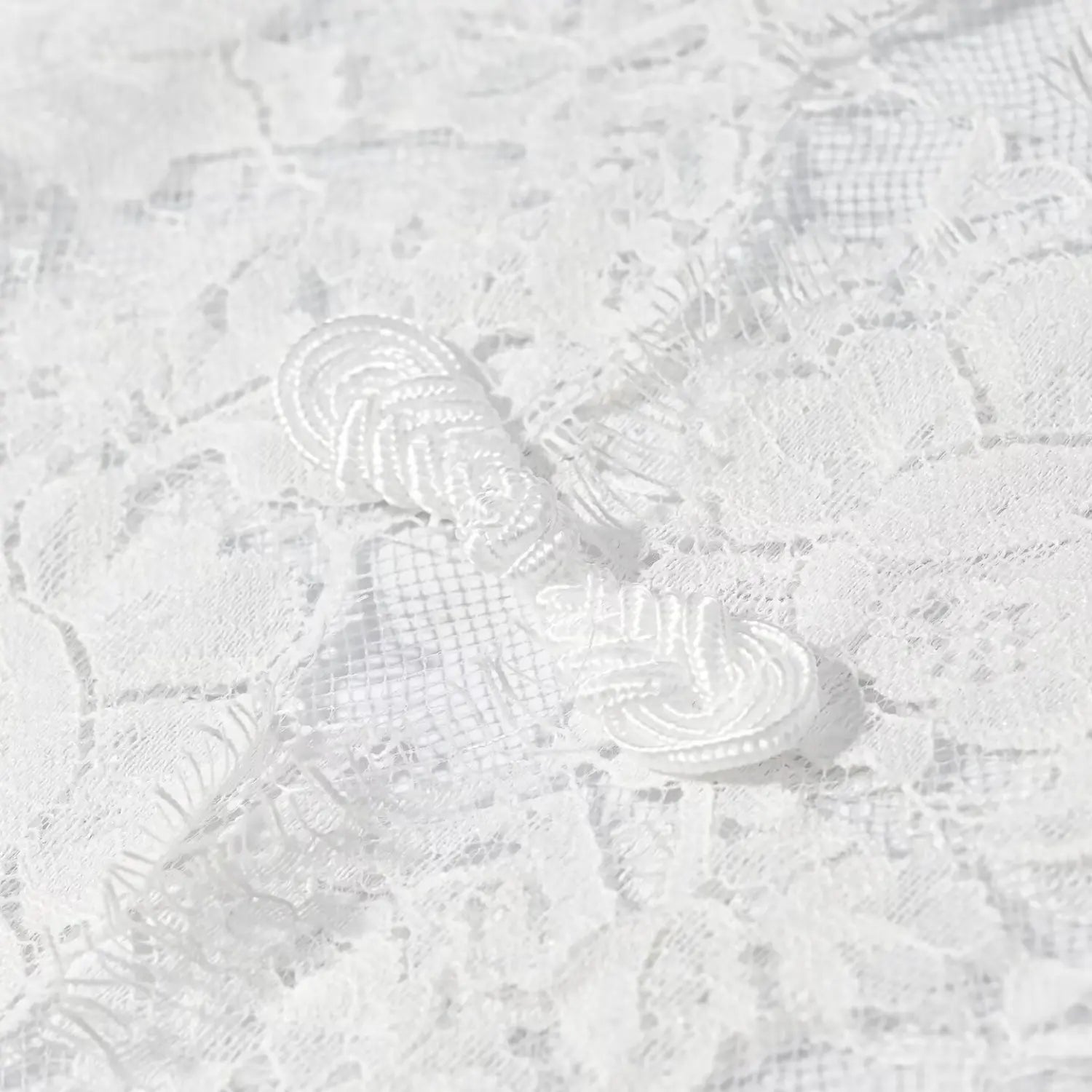 Extreme close‑up traditional frog knot button on white floral lace fabric