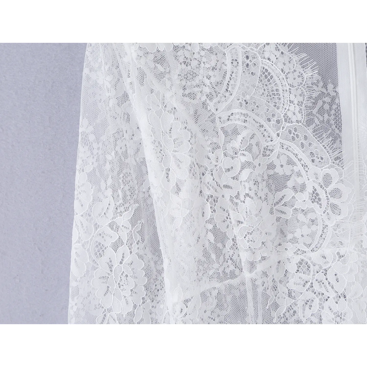 Macro close‑up of ornate flower lace texture on long sleeve of white mini dress