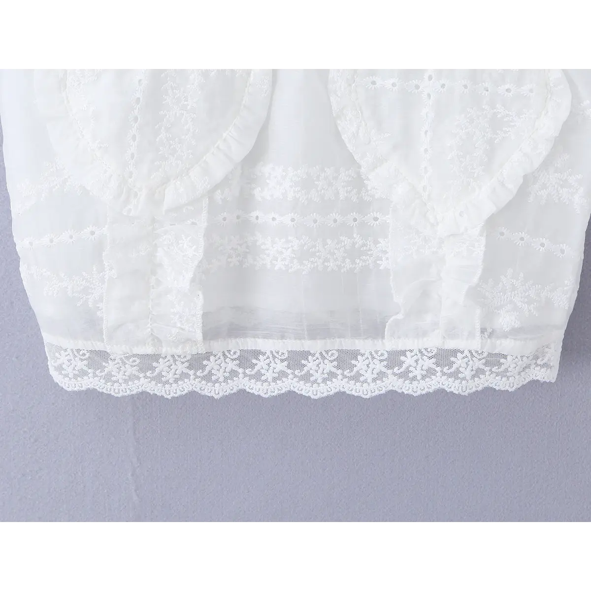 Close-up of the cropped hem, showing the delicate floral lace trim and embroidered border.