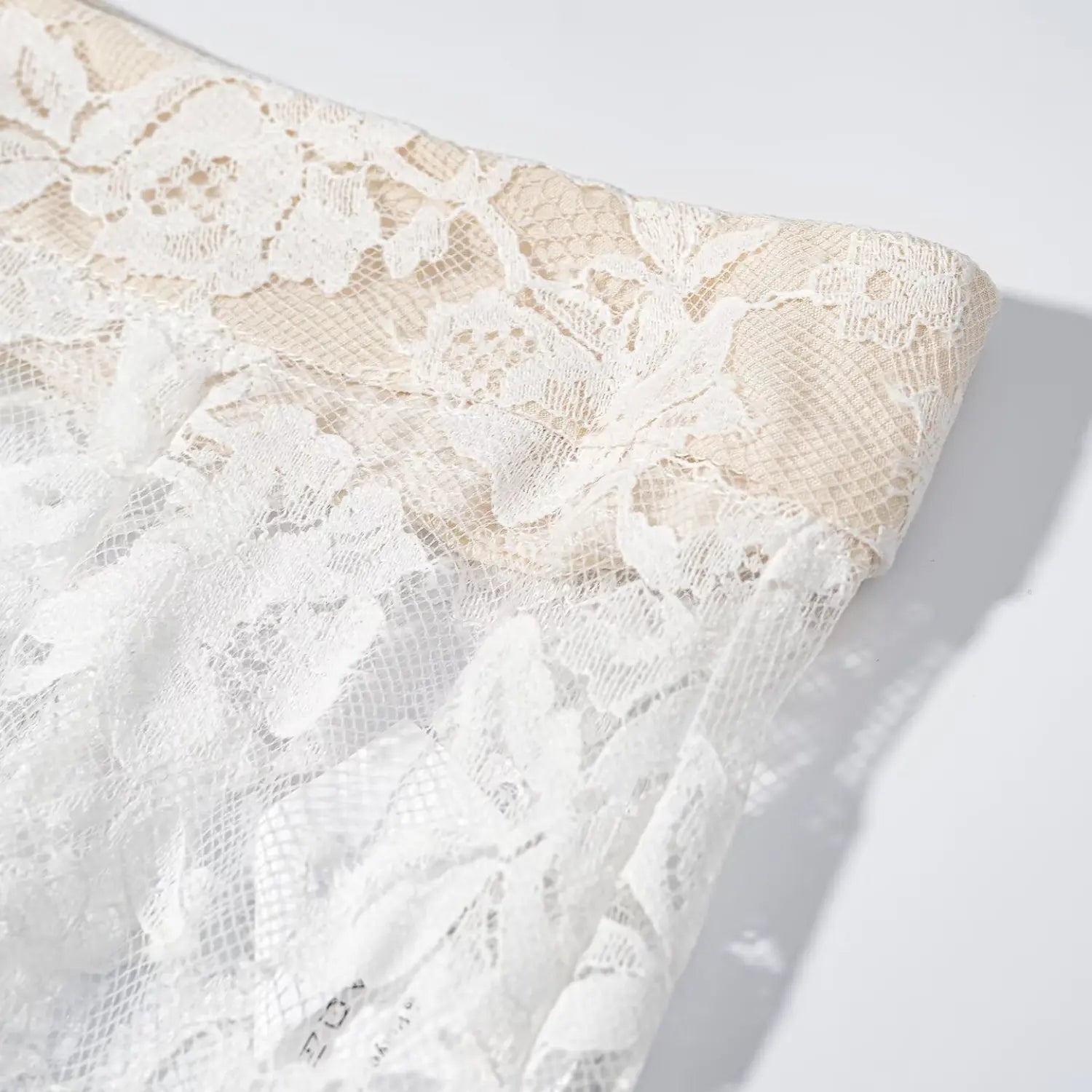 Close‑up seam detail beige waistband combined with outer white floral lace