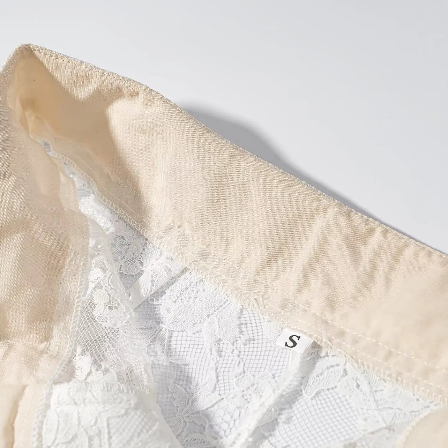 Close‑up inner beige waistband stitching and S size label tag of white floral lace wide leg trousers
