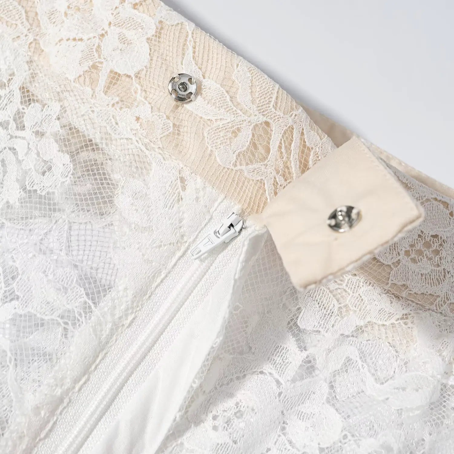 Close‑up side closure white zipper and metal snap button on white lace wide leg pants