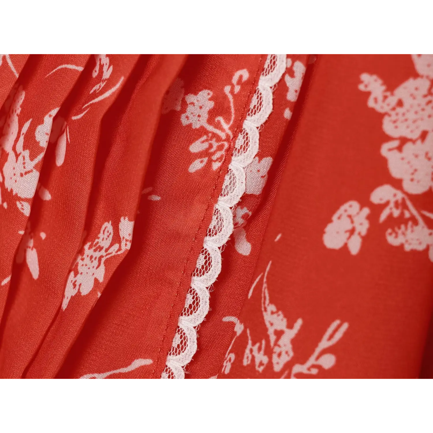 Macro close-up of delicate white lace piping trim on red floral chiffon dress