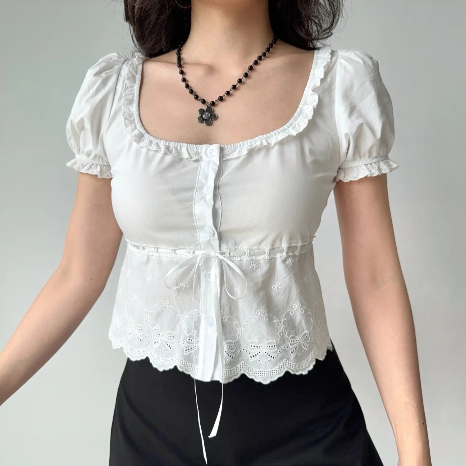 Lifestyle shot of a woman in a white lace-trimmed puff sleeve top with a bow tie detail at the waist