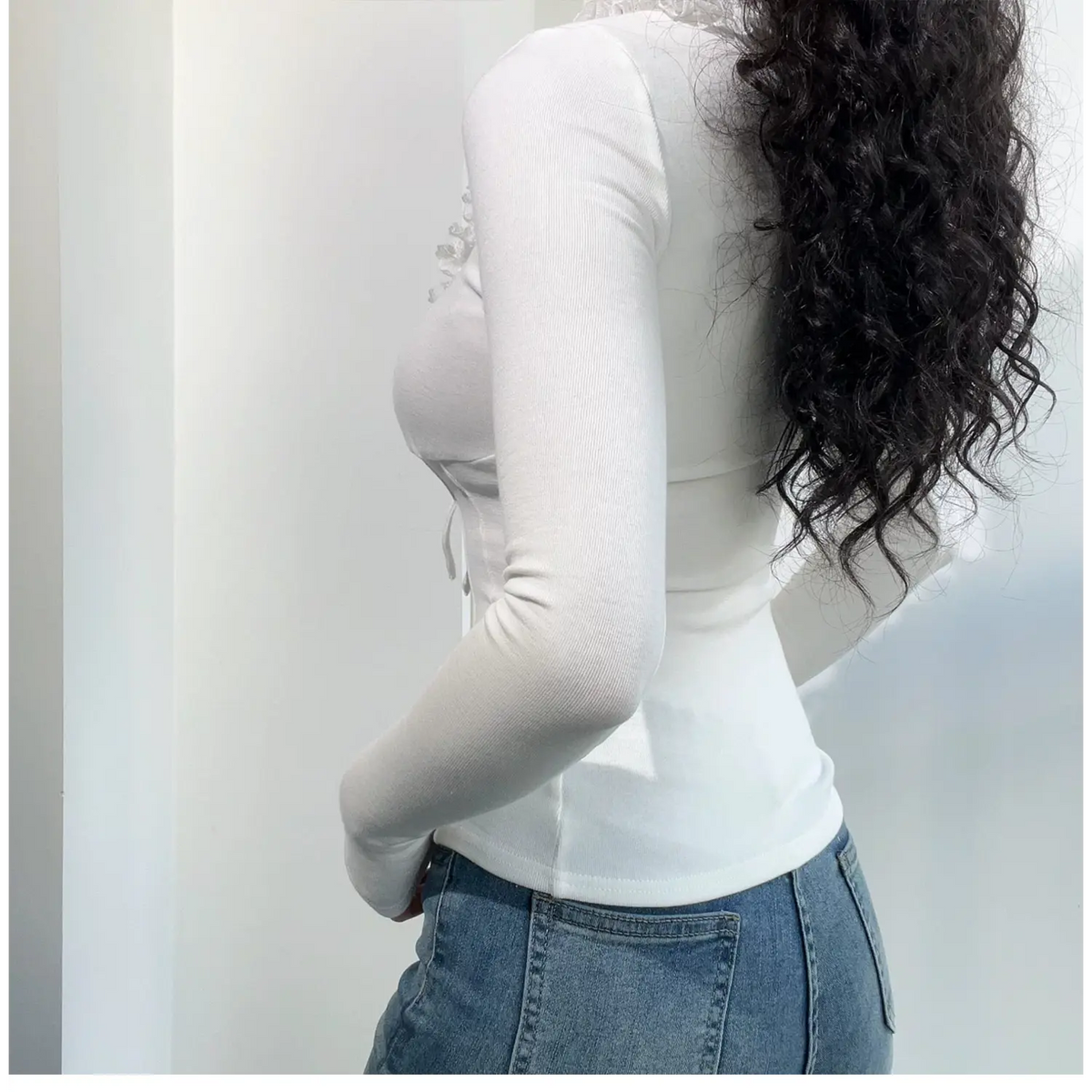Side view of white fitted long sleeve top, showing curved waist silhouette and stretch ribbed fabric