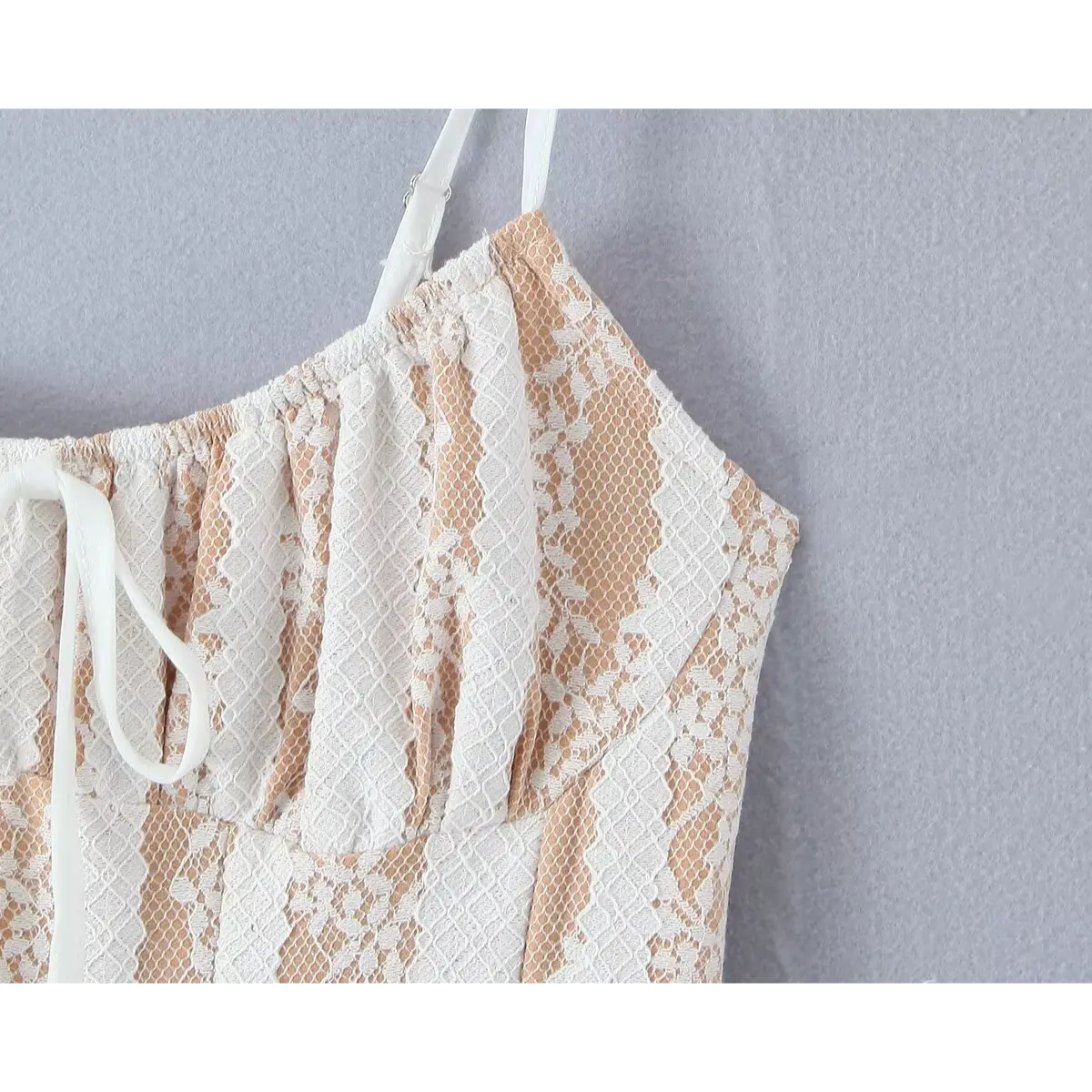 Close-up detail shot of the gathered bust and front tie on a white lace spaghetti-strap dress, showing the floral lace pattern.