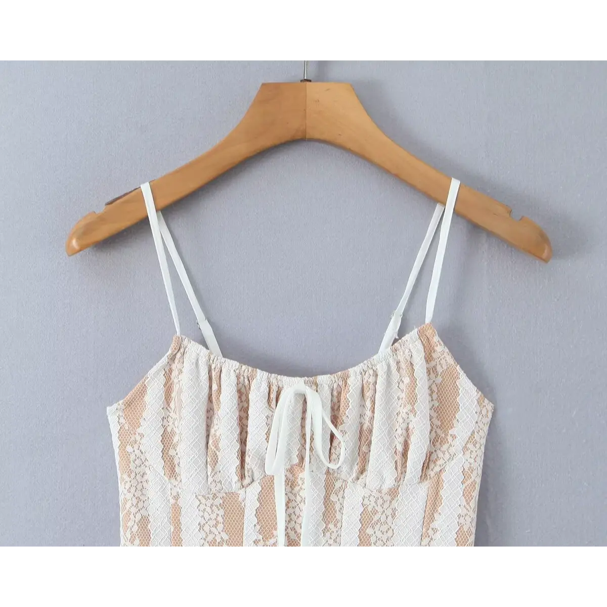 Front view of a white lace spaghetti-strap dress on a wooden hanger, showing the gathered bust, front tie, and adjustable straps.