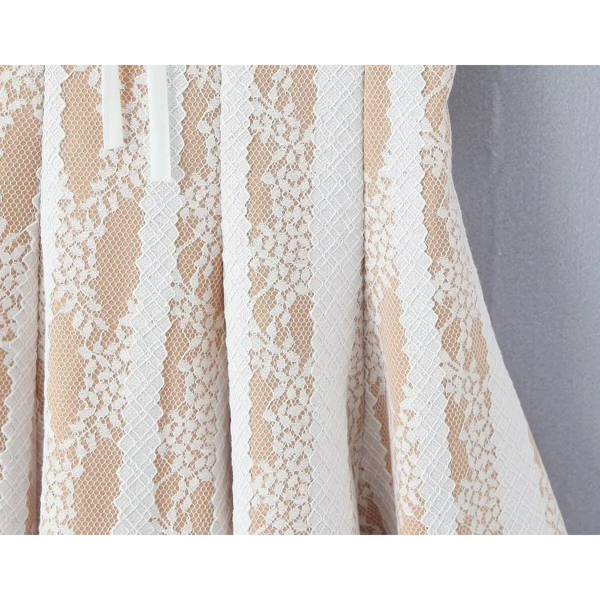 Close-up detail shot of the vertical floral lace pattern on a white lace spaghetti-strap dress, showing the nude lining underneath.
