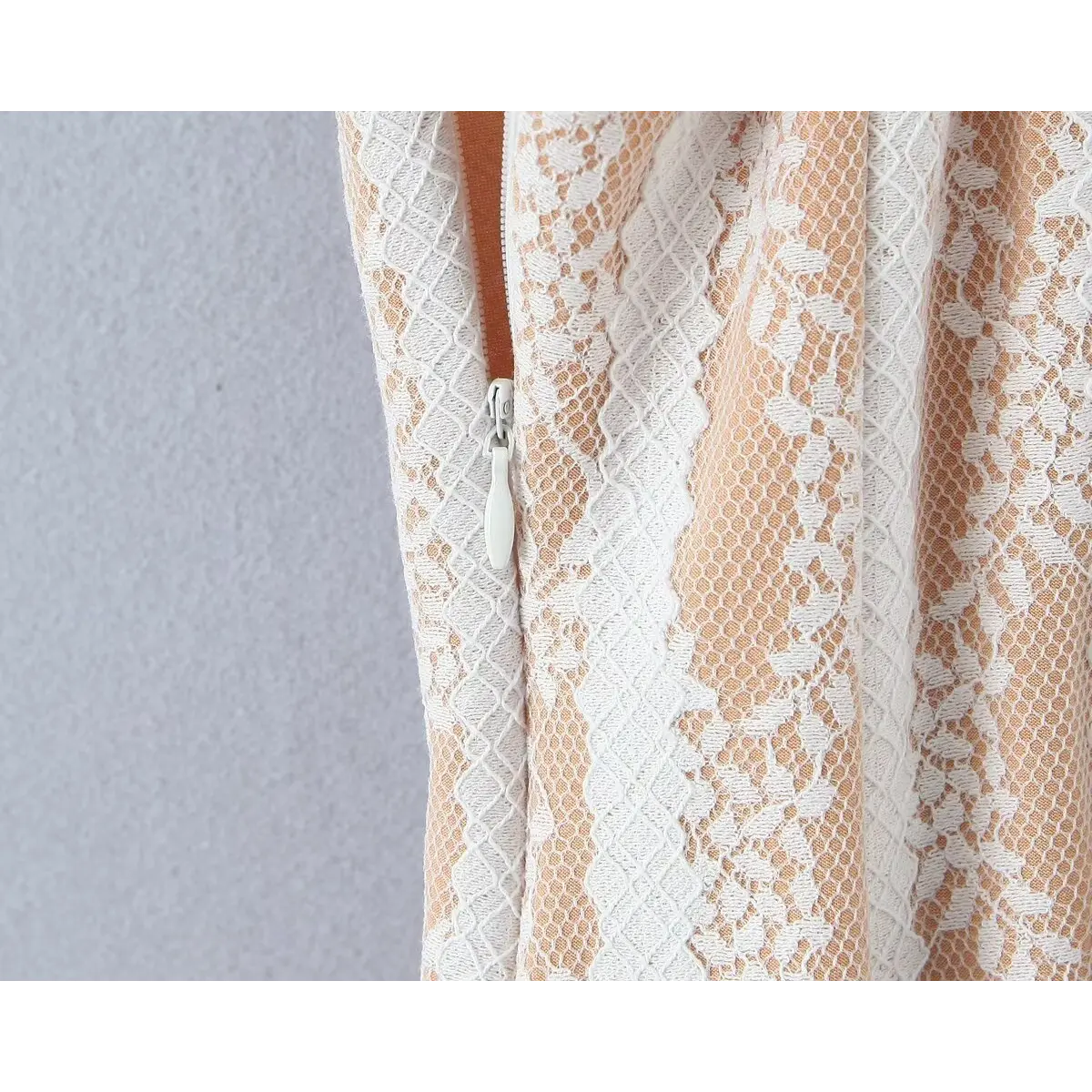 Close-up view of the side zipper on a white lace spaghetti-strap dress, showing the white zipper pull and nude lining.