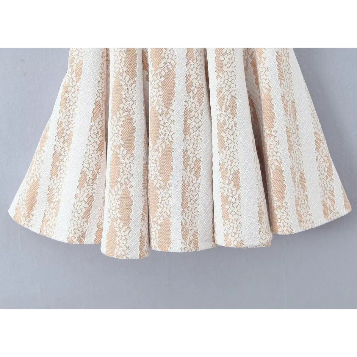 Close-up detail shot of the flared skirt hem on a white lace spaghetti-strap dress, showing the vertical floral lace stripes.