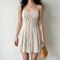 Model wearing a white lace spaghetti-strap mini dress with nude lining and center drawstring, styled with a pearl necklace and wicker handbag, front view.