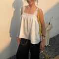 Woman wearing white lace square neck linen camisole top, outdoor street front view, casual summer outfit with black trousers and yellow shoulder bag