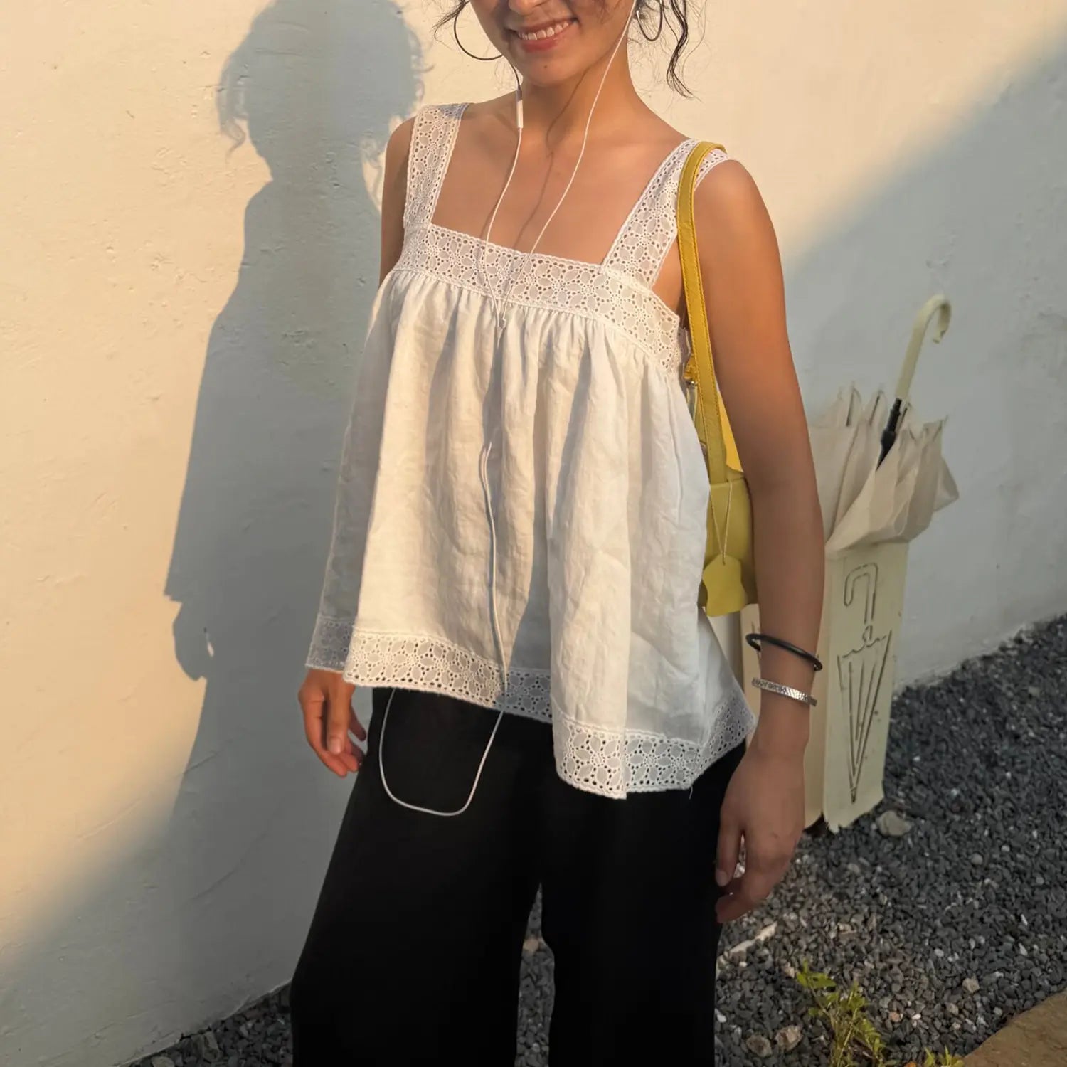 Woman wearing white lace square neck linen camisole top, outdoor street front view, casual summer outfit with black trousers and yellow shoulder bag
