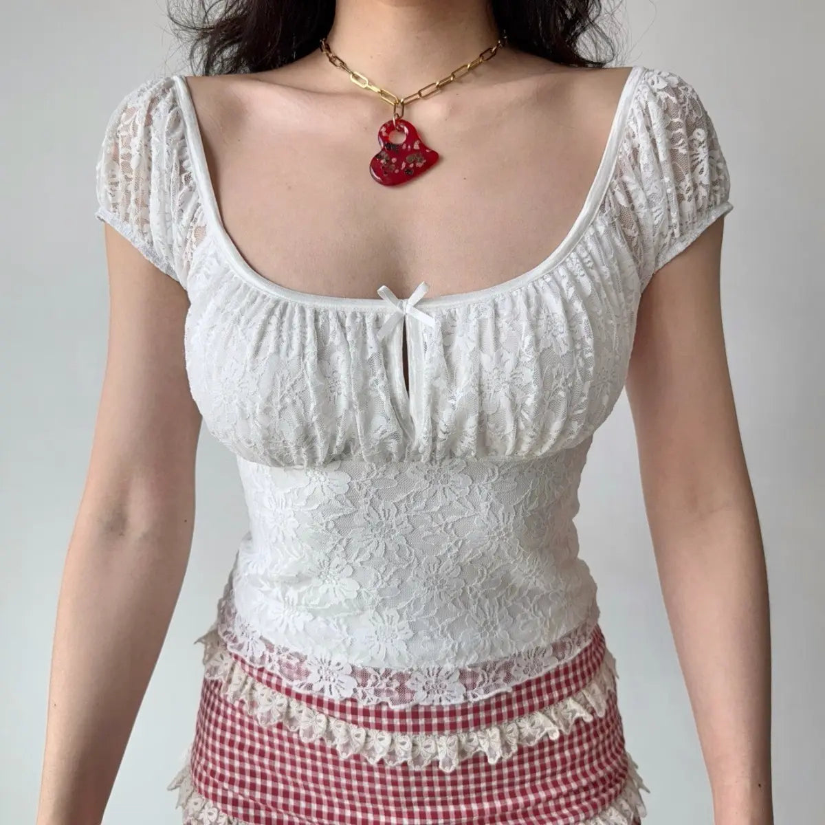 The lace top styled with a chunky gold chain and red heart pendant, emphasizing the neckline.