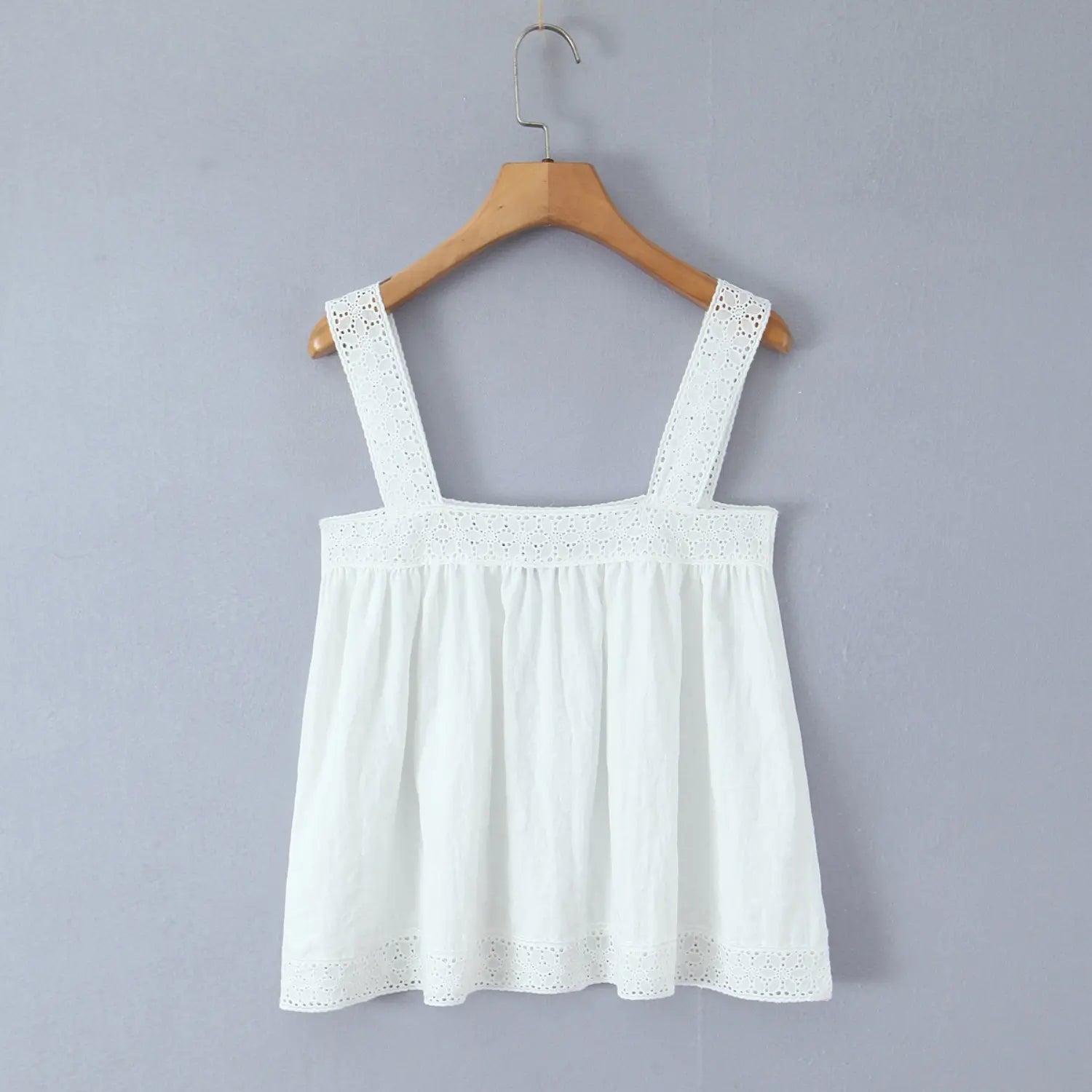 White loose square neck camisole with eyelet lace trim hanging on wooden hanger against light gray background
