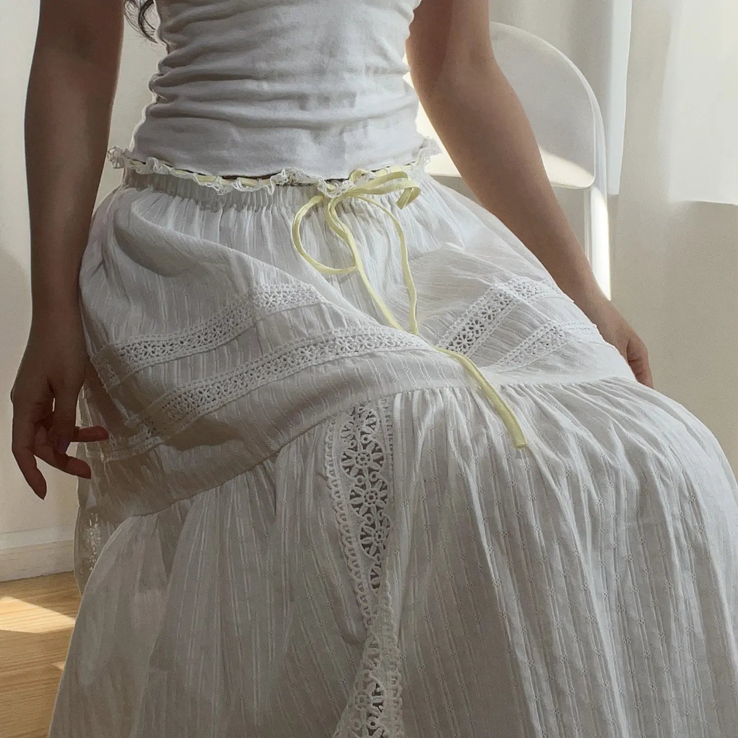 Close-up of the waistband on the white lace tiered maxi skirt, featuring a ruffled edge and yellow drawstring tie.