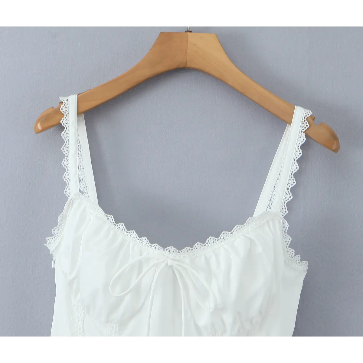 Partial view on wooden hanger of the white dress showing lace straps, neckline, and front bow detail