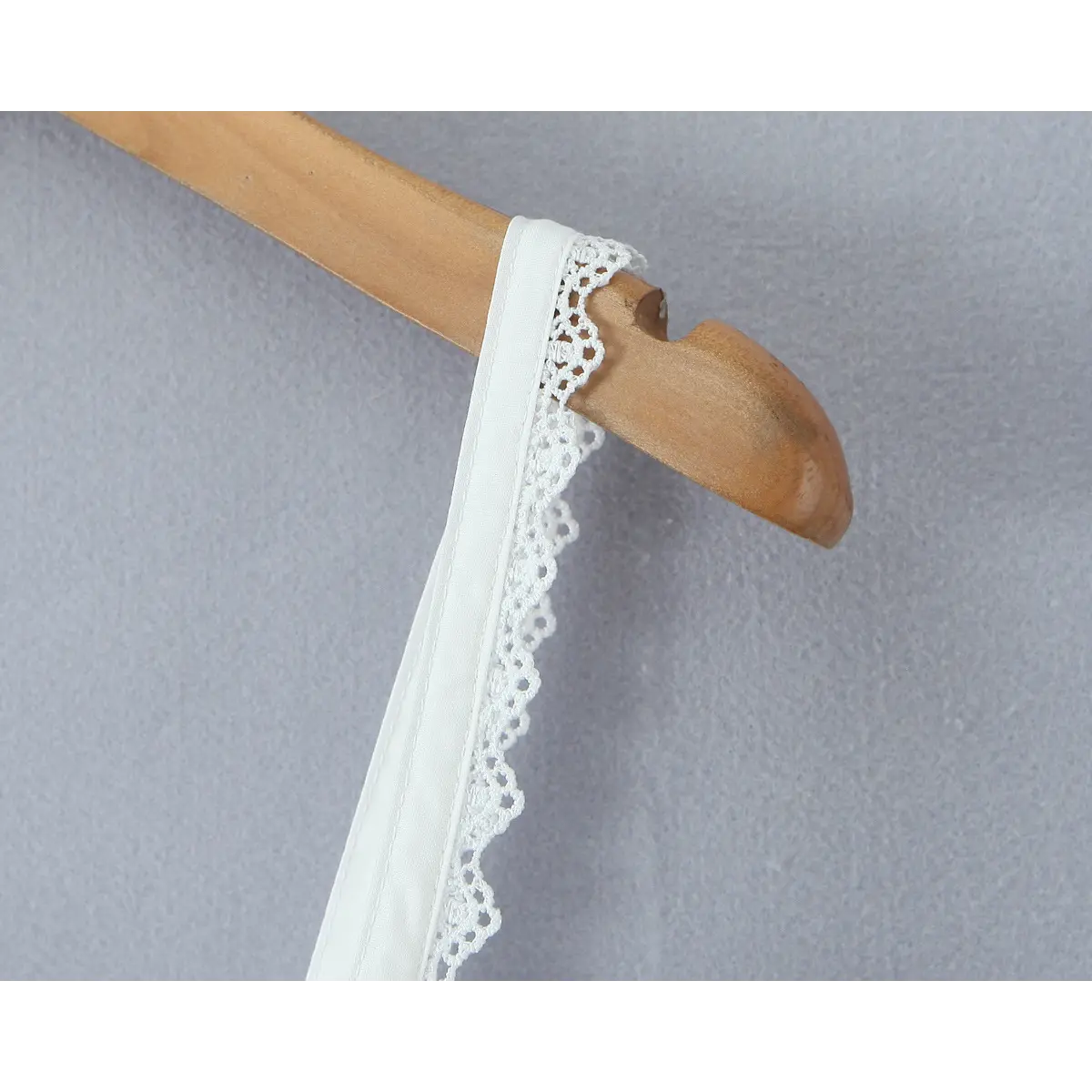 Close-up of the adjustable spaghetti strap trimmed with scalloped lace on the white dress