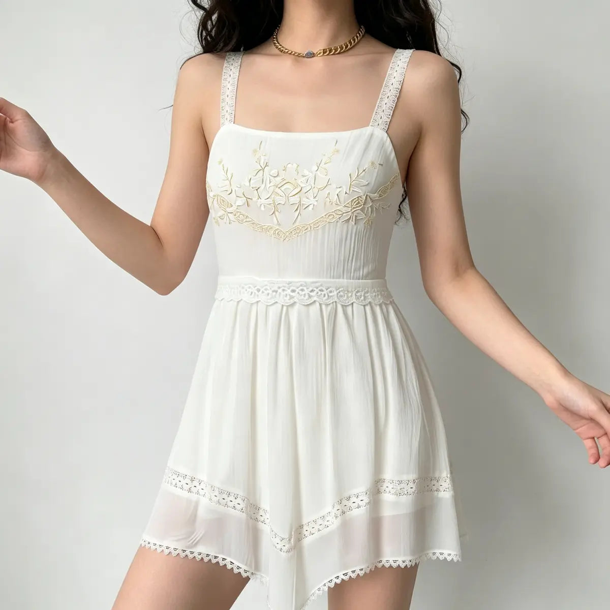 Model in white cami dress with delicate lace straps, gold embroidery, and tiered lace hem.