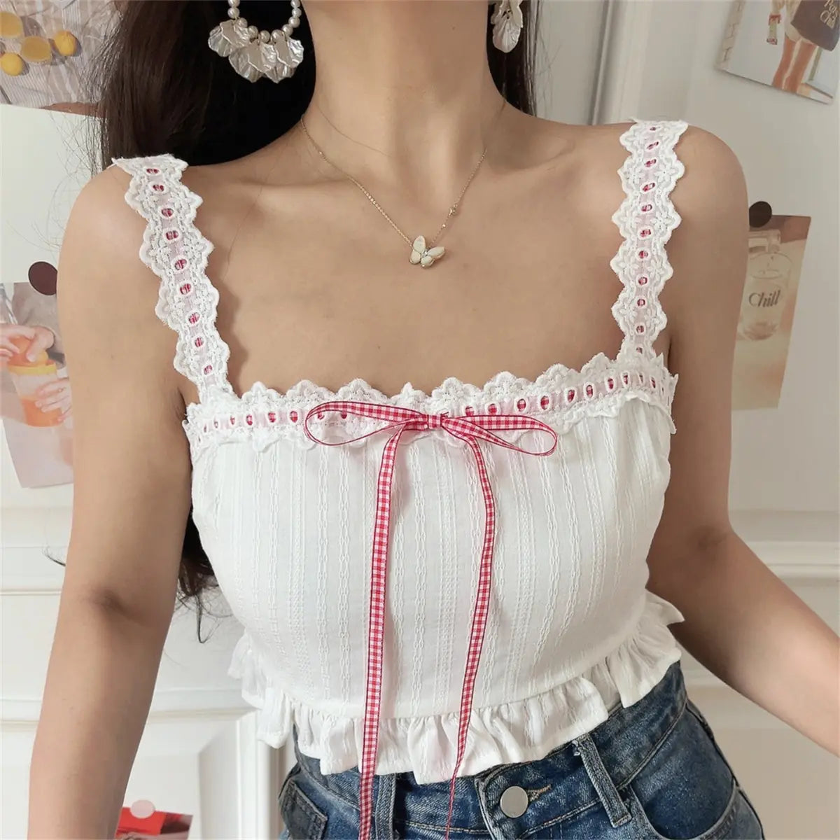  Angled view of a woman wearing a white lace-trimmed camisole top with a red gingham ribbon bow, paired with jeans.