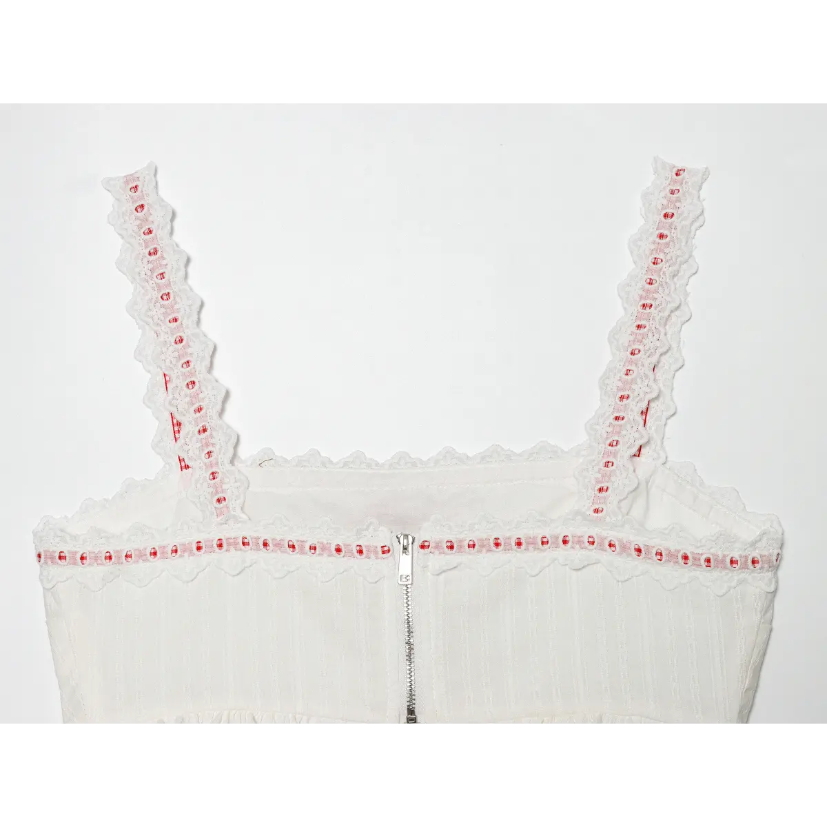 Close-up detail of the silver zipper closure and lace-trimmed bust on the back of a white camisole, isolated on a white background.