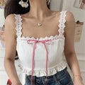Close-up view of a woman wearing a white lace-trimmed camisole top with a red gingham ribbon bow, paired with jeans.