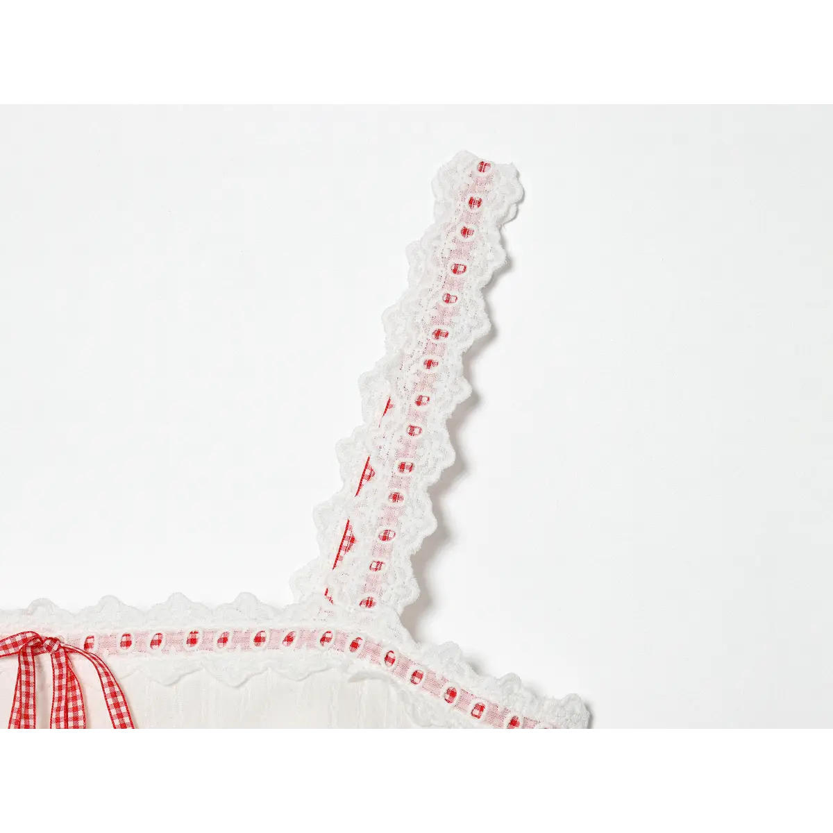 Close-up detail of a lace-trimmed strap on a white camisole, showing the red gingham ribbon woven through the eyelet lace.