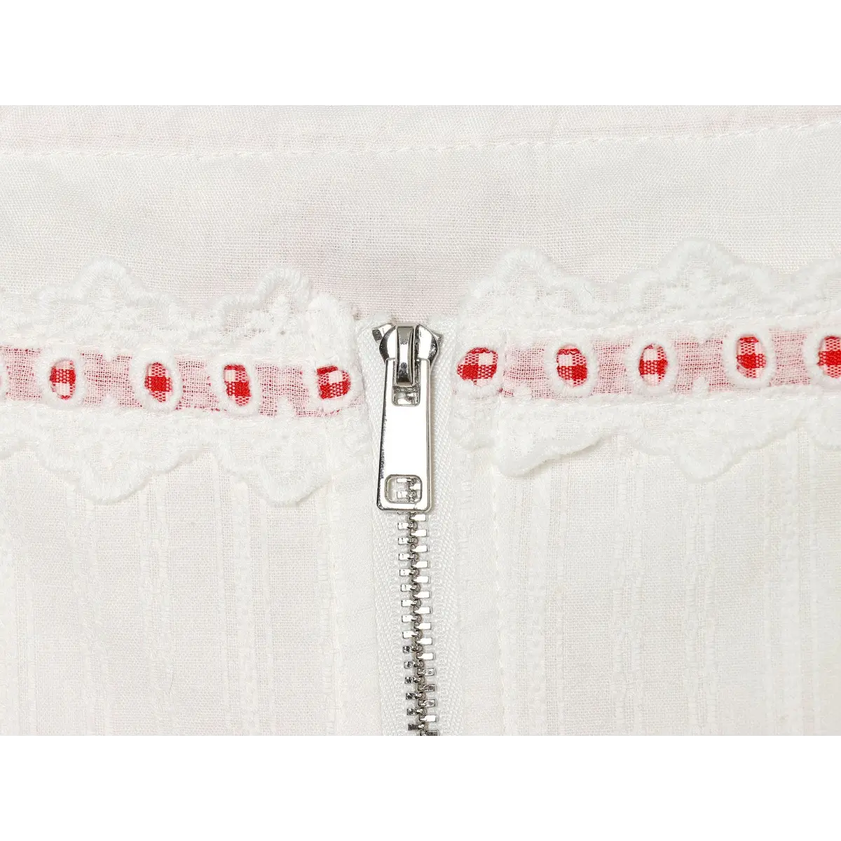 Close-up detail of the silver zipper pull and lace trim on the back of a white camisole, highlighting the red gingham accents.
