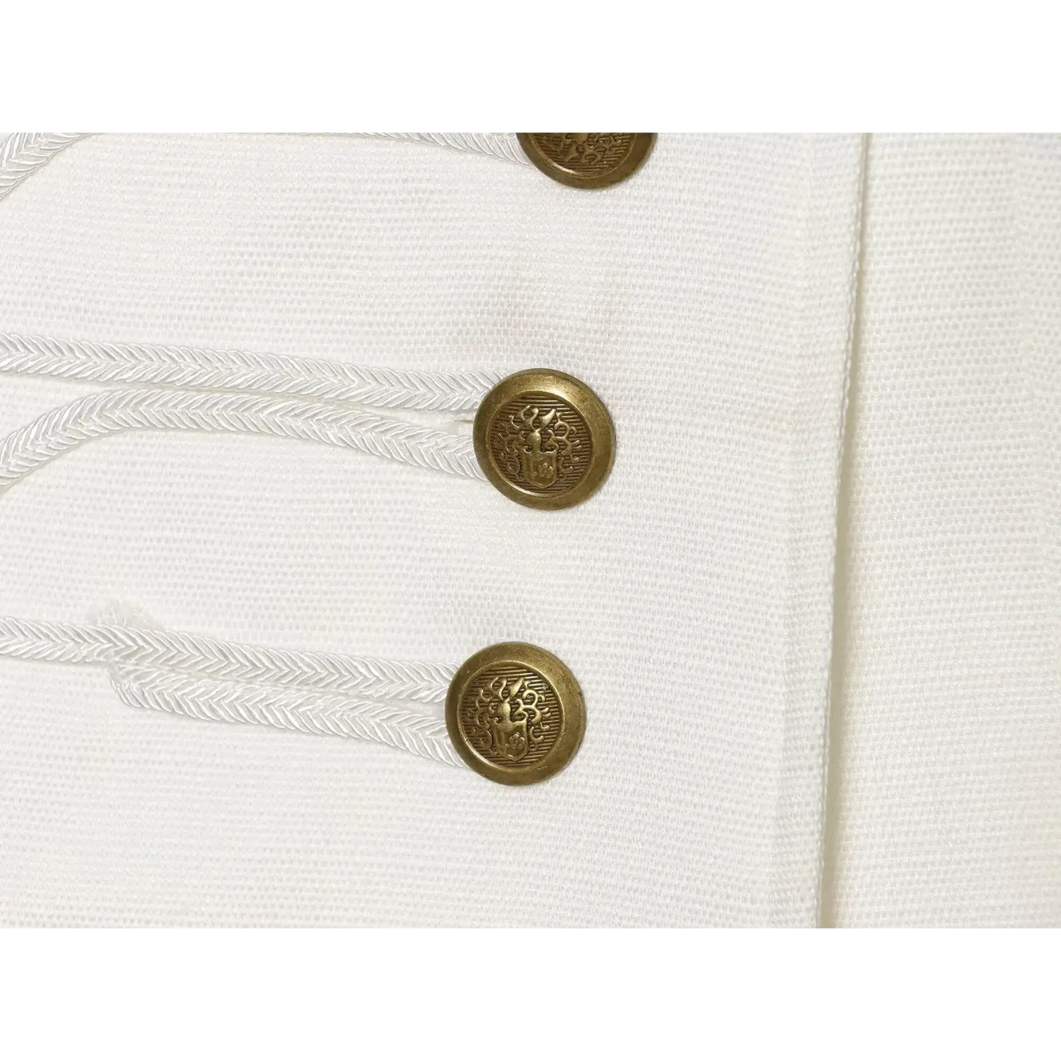 Macro close‑up of embossed antique brass buttons and braided cord trim on white woven dress