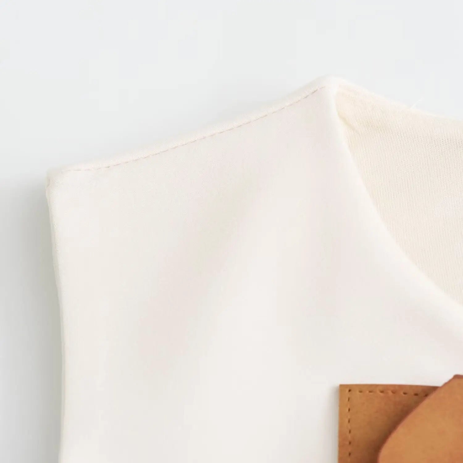 Close‑up of armhole and neckline neat stitching on smooth white woven sleeveless dress