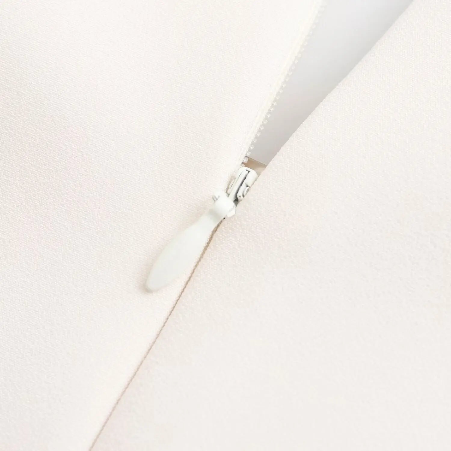 Close‑up shot of invisible back zipper with fabric pull tab on white structured sleeveless mini dress