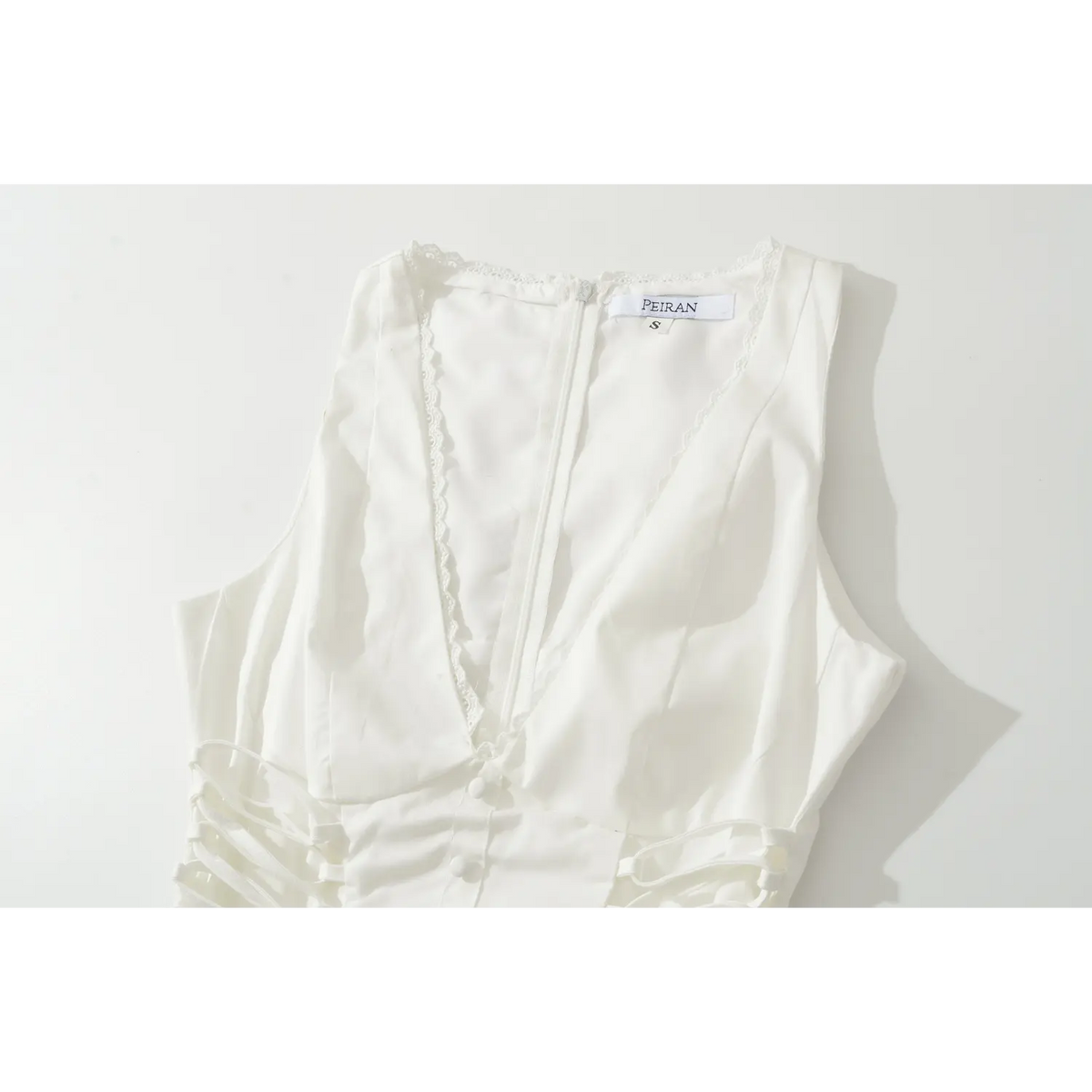 Close-up of white corset dress deep v neckline, delicate lace trim, side lace-up ties and fabric covered buttons