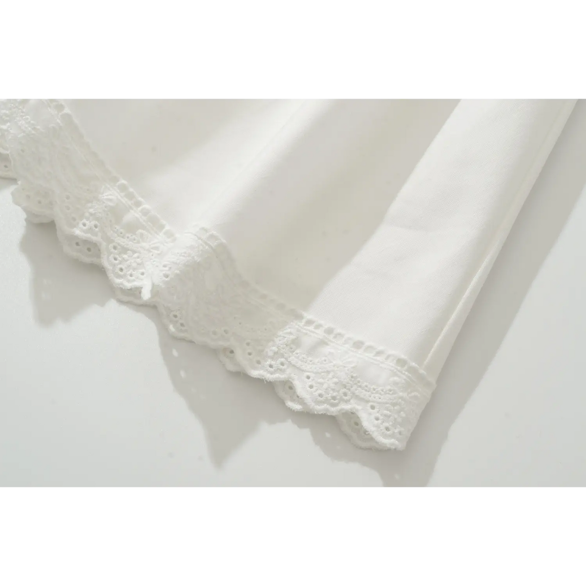 Close view of scalloped eyelet lace hem and soft woven fabric of white corset mini dress