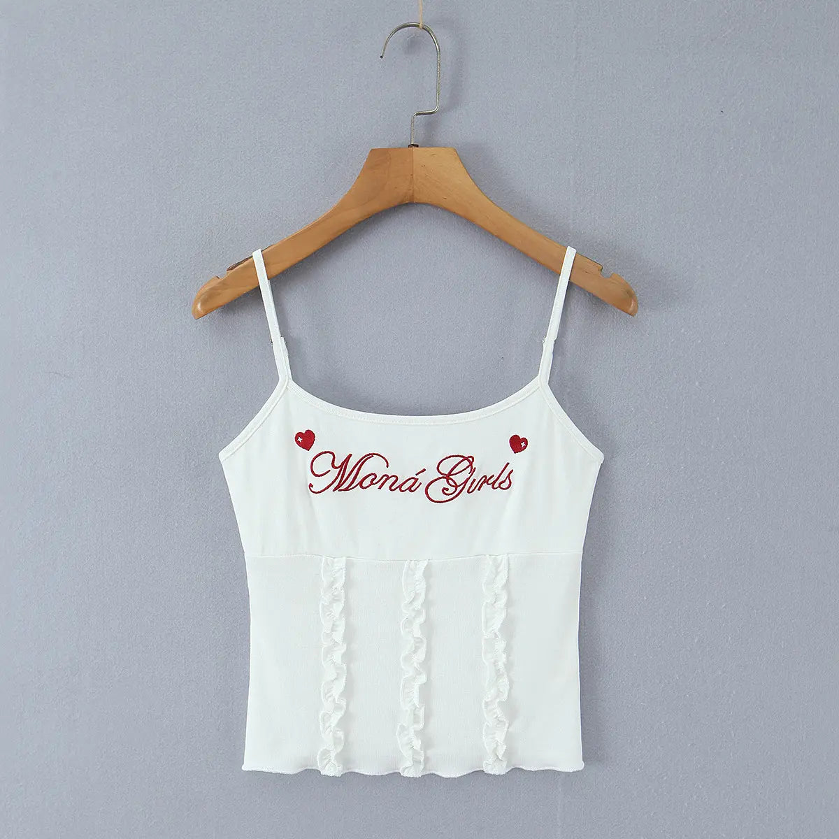 Full front view of the cami top, featuring red embroidered text "Moná Girls", two small red hearts, and vertical ruffled details at the hem.