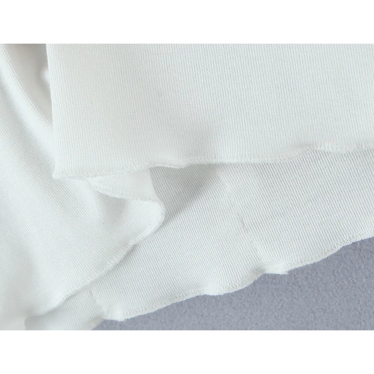Close-up of the fabric, showing the fine ribbed knit texture and the lettuce-edge hem finish.