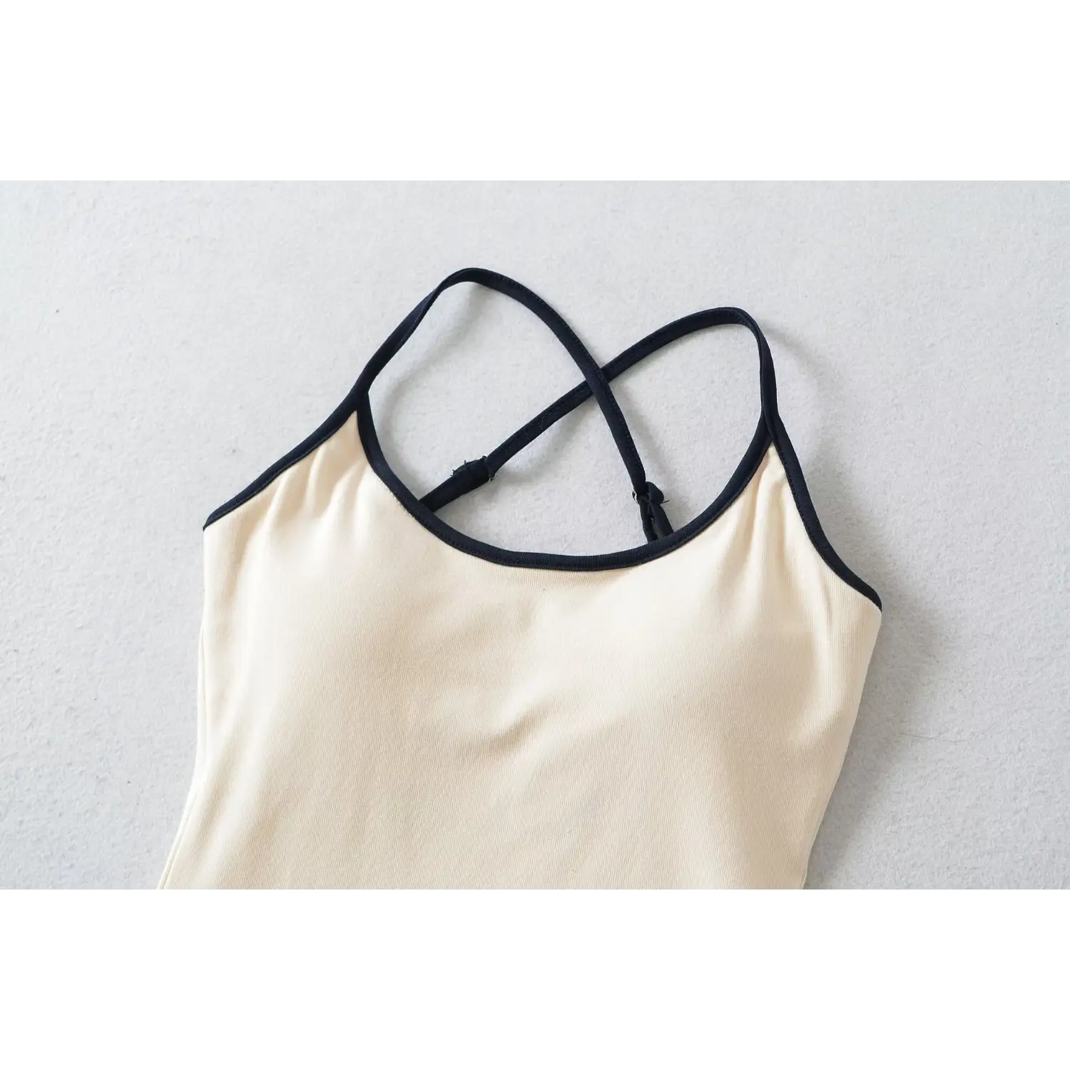 Close-up of beige camisole with black trim and adjustable crisscross straps, part of white navy striped two piece outfit