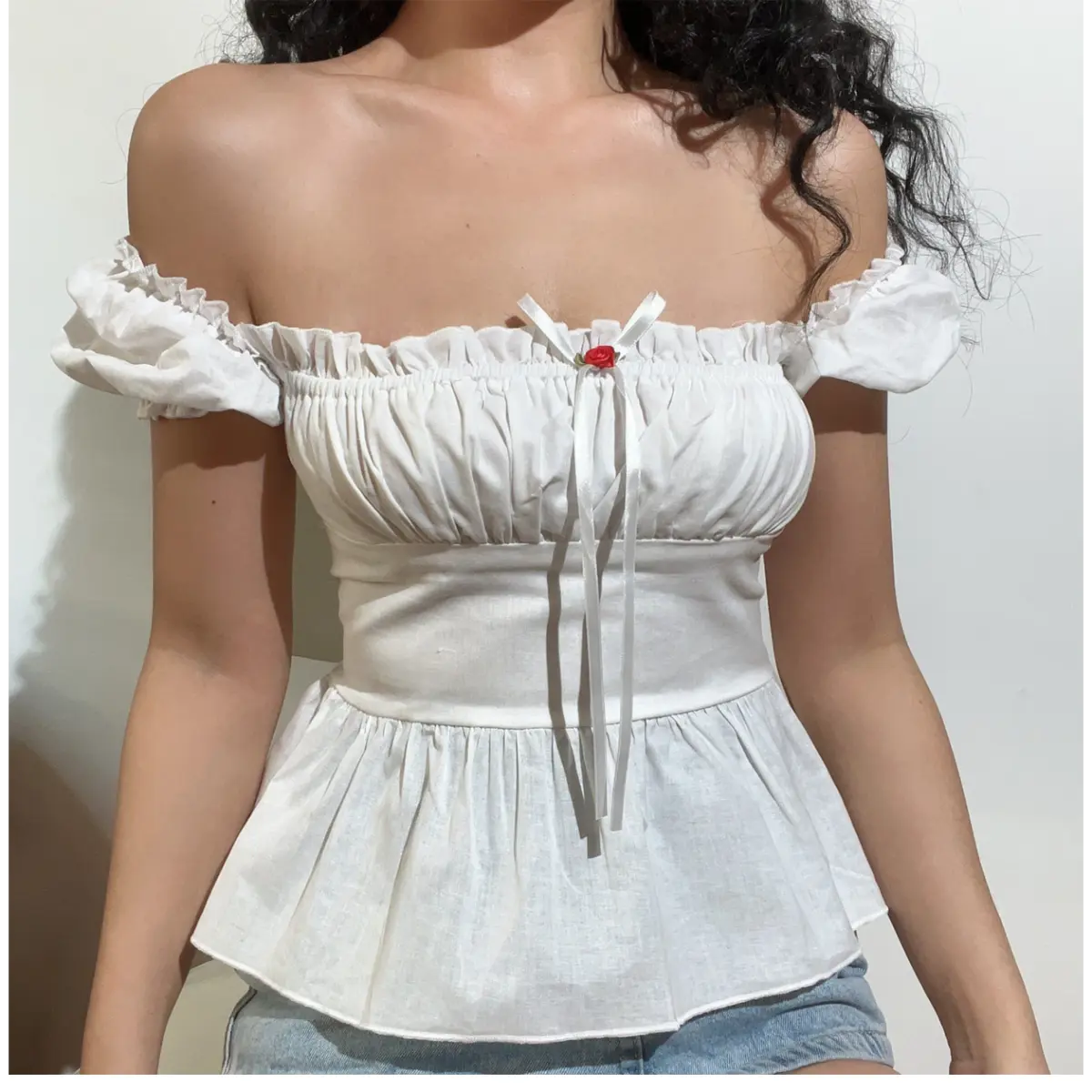 Front view of a white off-shoulder peplum top, highlighting the square neckline, ribbon bow with rose accent, and fitted waist.