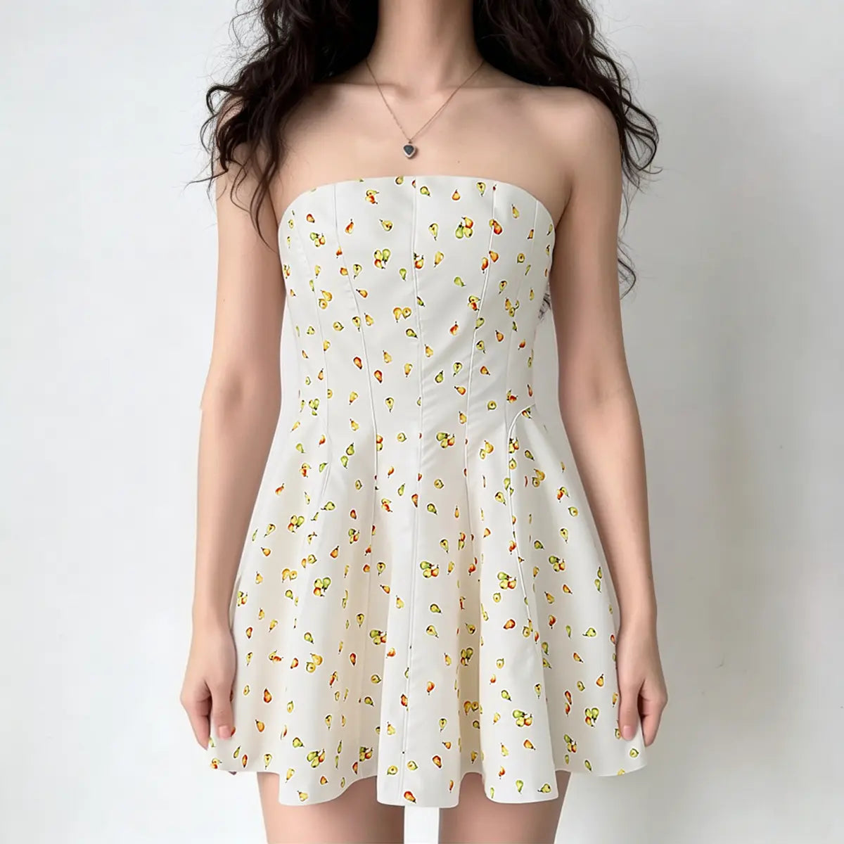 Model wearing a white strapless mini dress with watercolor pear print, featuring a structured bodice and flared skirt, front view.