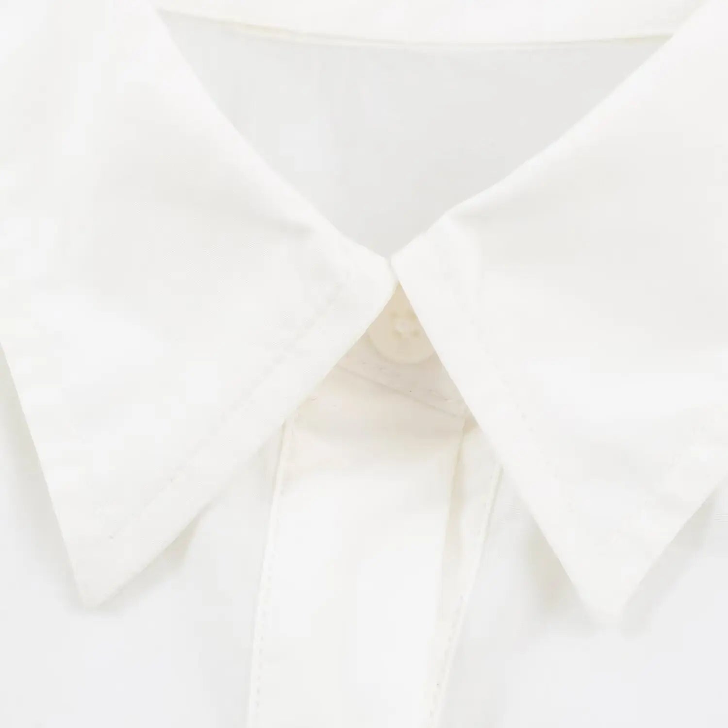 Extreme closeup pointed collar and top button of white fitted peplum blouse