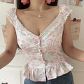 Women white pink floral lace cami crop top, fitted waist ruffle hem button detail, half body shot against white wall
