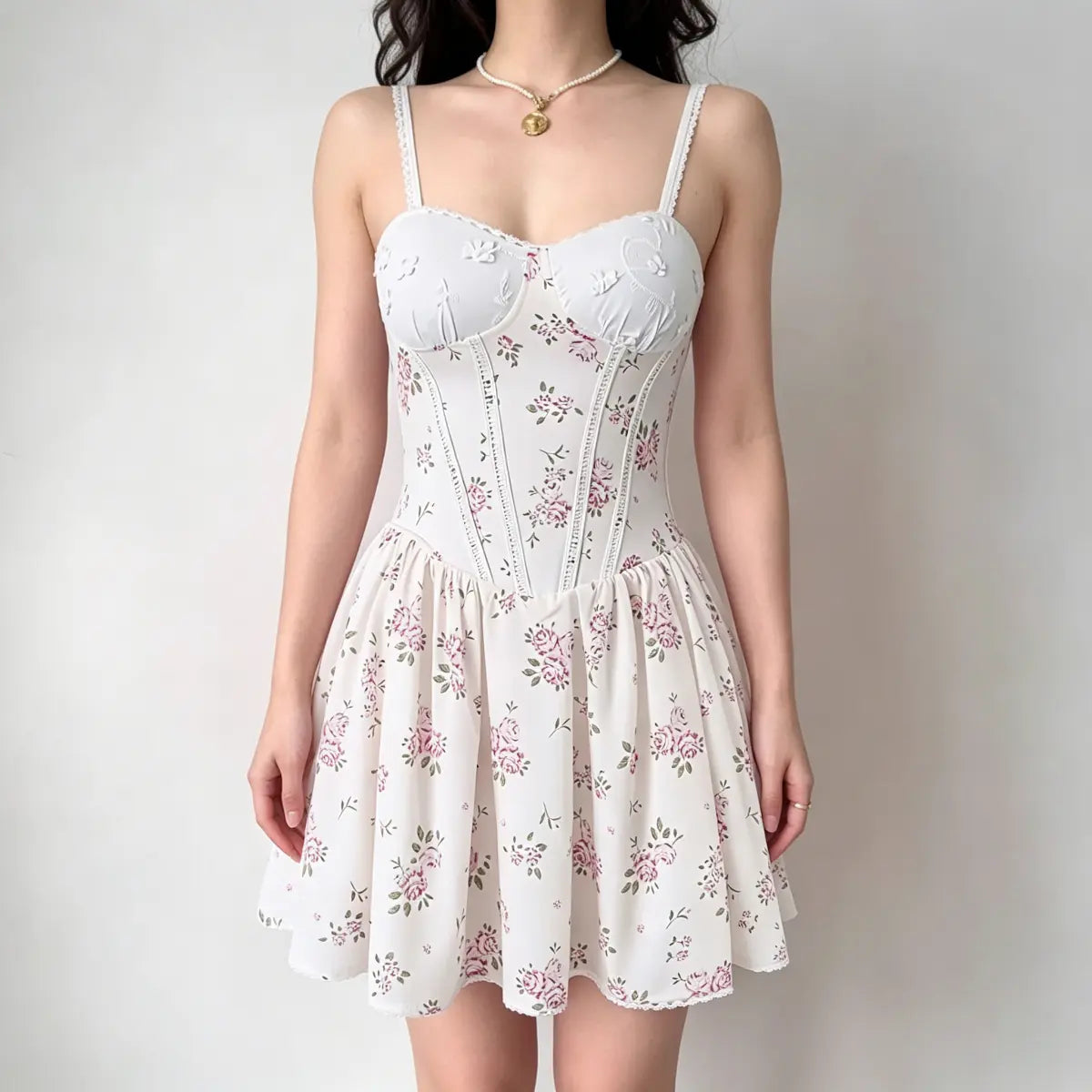 Model wearing a white corset-style mini dress with a pink rose print, featuring lace-trimmed spaghetti straps and a flared skirt.