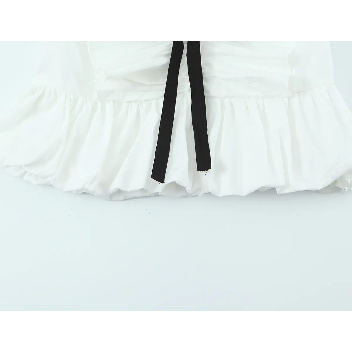 Hem view of the white ruffle top, showing the puffy bubble hem and center black ribbon tie